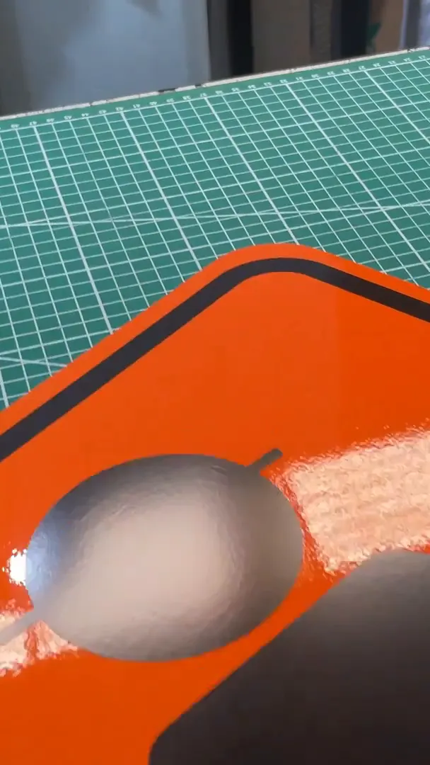 Tablero de obra en reflejante naranja con su filete negro, sobre la mesa de corte del taller de Nyne Print